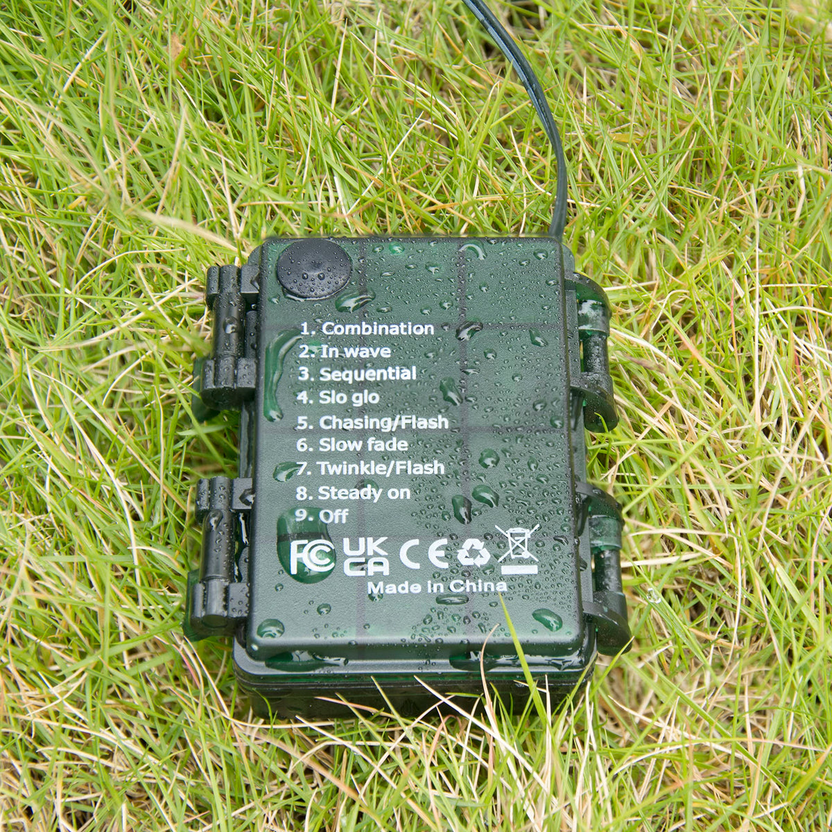 Green IP65 waterproof battery case covered in water drops lying on grass with 9 mode labels