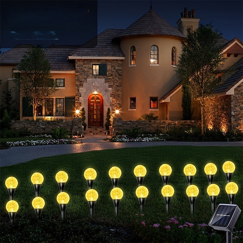 Warm white solar crystal bubble ball garden stake lights glowing at night in front of a stone villa