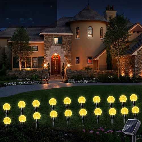 Warm white solar crystal bubble ball garden stake lights glowing at night in front of a stone villa